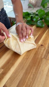 Hands folding a tortilla wrap on a wooden table.