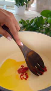 Stirring tomato paste into oil in a pot with a wooden spoon.