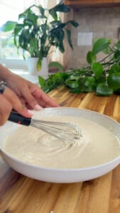 Person whisking salad dressing in a white bowl.