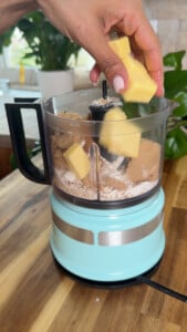 Adding butter to food processor with flour and brown sugar.