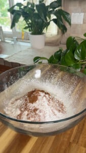 Mixing bowl with flour and cinnamon powder on a wooden countertop.