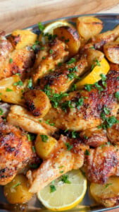 Roasted chicken with potatoes, lemon, and fresh herbs on a platter.