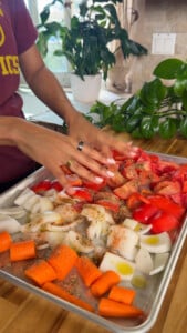 Chopped vegetables with seasoning on a baking tray include tomatoes, onions, and carrots.