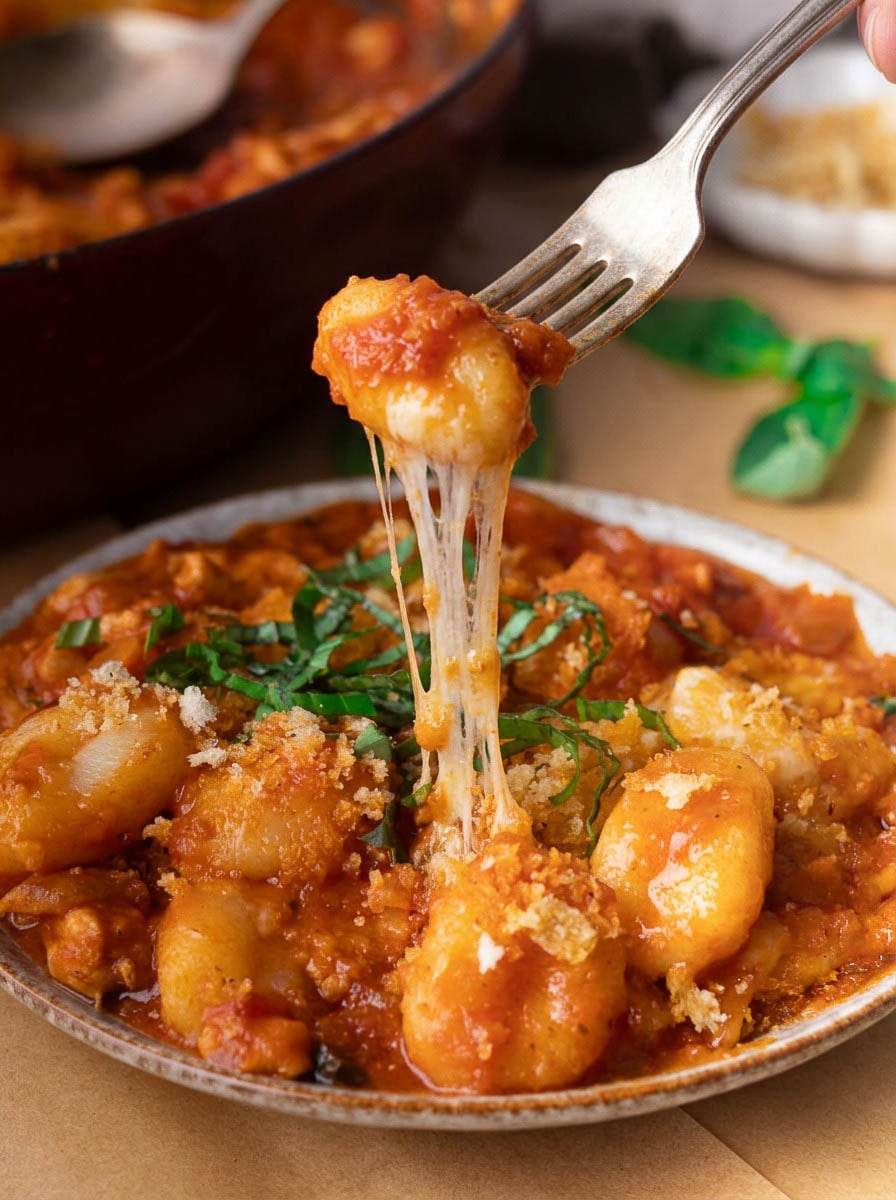 Cheesy gnocchi chicken parm with basil, served hot in a dish, close-up.