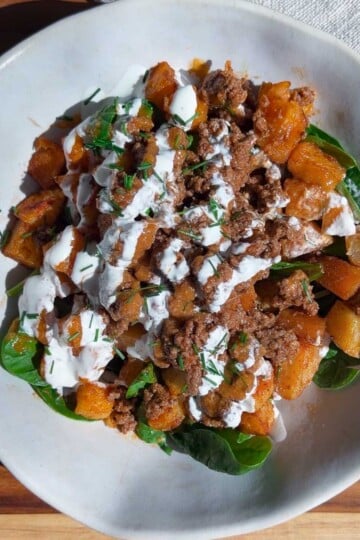 Patata brava bowl with ground beef with herbs and creamy drizzle on a wooden table.