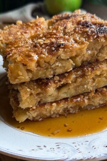 Stack of sheet pan apple crumble pancakes drizzled with syrup on a white plate.