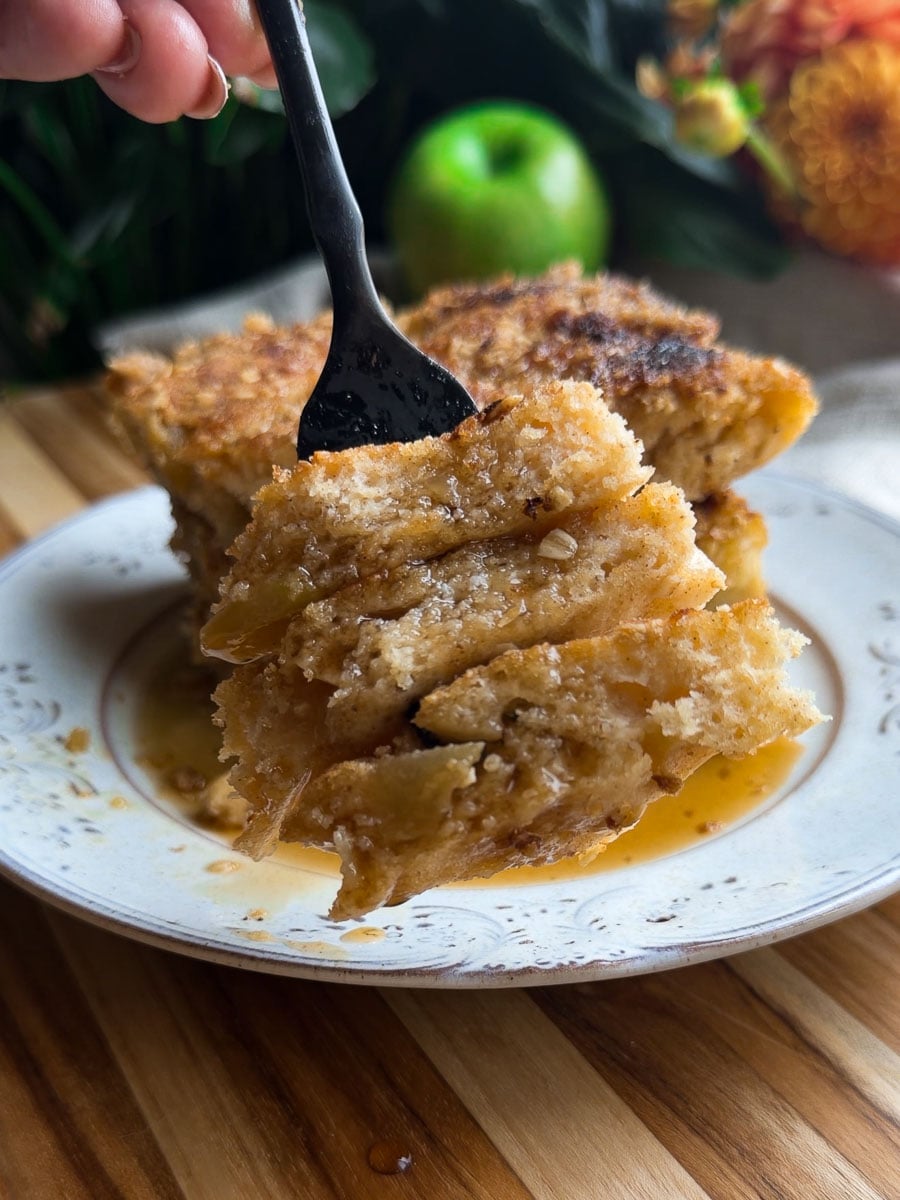 Close-up of sheet pan apple crumble pancakes slice on a fork with syrup, served on a decorative plate.
