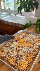 Baking tray with cheesy potatoes in a cozy kitchen setting by a window with plants.