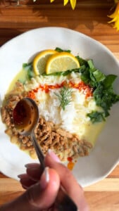 Plate of rice with minced meat, lemon slices, and greens, garnished with sauce; hand holding a spoon.