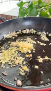 Chopped onions and minced garlic sautéing in oil in a black skillet.