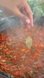 Adding bay leaf to simmering sauce in a skillet.