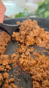 Sizzling ground beef on skillet with spoon close-up.
