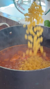 Pasta shells being added to a pot of tomato sauce