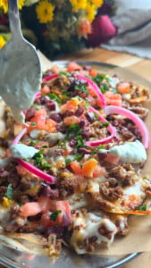 Loaded potatoes with toppings and tzatziki being added, garnished with herbs and fresh vegetables.