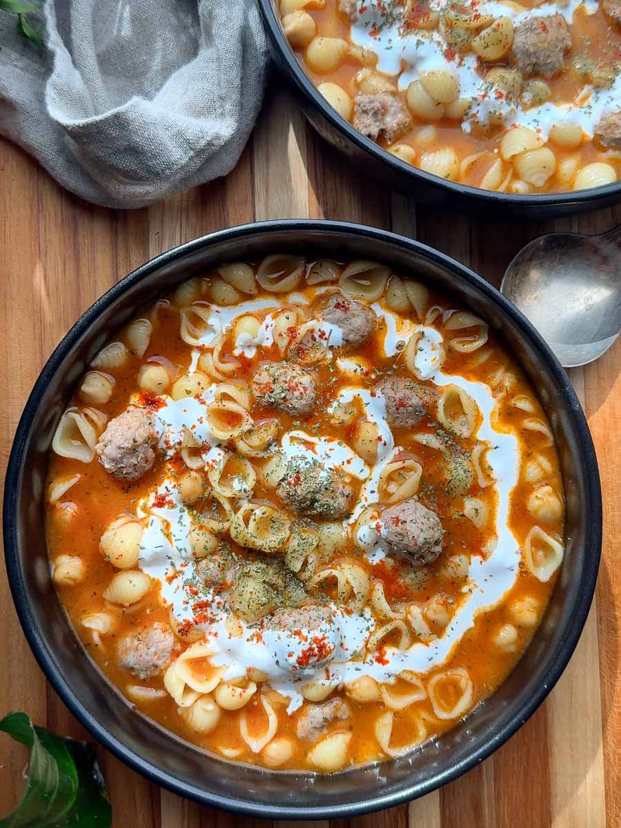 Armenian meatball soup with shell noodles, meatballs, tomato broth, and a swirl of cream.
