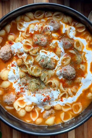 Armenian meatball soup with pasta shells, meatballs, and a swirl of cream in a bowl