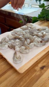 Person seasoning raw shrimp on a wooden cutting board in a kitchen setting.