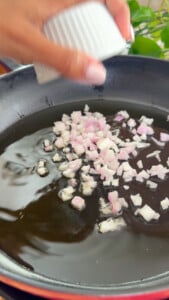 Chopped shallots being added to a hot pan with oil for cooking.