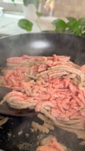 Cooking ground chicken in a pan with steam rising, close-up shot.