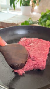 Cooking ground beef in a skillet with a wooden spatula in a bright kitchen.