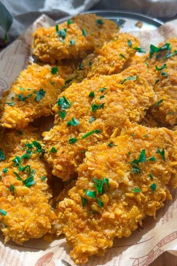 Crispy baked chicken tenders topped with chopped parsley on a tray.