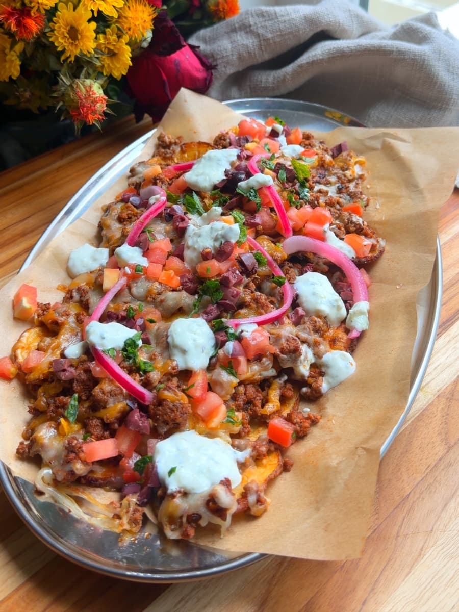 Greek loaded nachos topped with ground meat, tomatoes, onions, cheese, and garnished with cilantro.