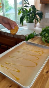 Drizzling olive oil on a parchment lined baking sheet, preparing to bake sliced potatoes.