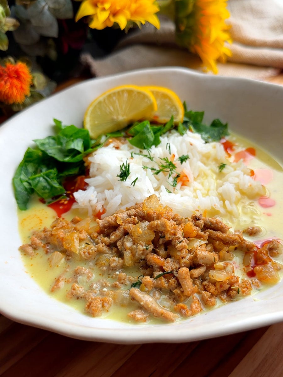 Bowl of Mediterranean brothy rice and chicken with spinach, minced meat, and lemon slices in a creamy sauce on a wooden table.