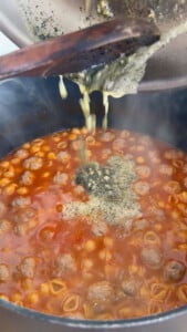 Pasta and meatballs simmering in tomato sauce in a pot