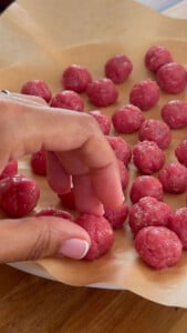 Hand shaping pink meatballs on parchment paper.