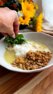 Hand adding spinach to rice and ground chicken.