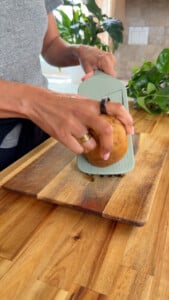 Person slicing potato on a wooden board with a mandoline slicer.