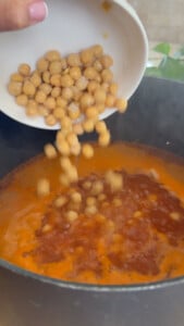 Chickpeas being added to a pot of simmering sauce