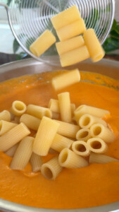 Rigatoni pasta being added to creamy orange sauce