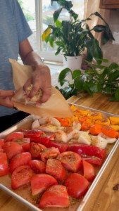 Seasoned chopped tomatoes, onions, carrots, and pumpkin on a baking sheet.