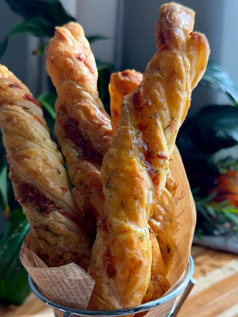 Twisted puff pastry baked breadsticks with golden, flaky crust in a metal basket