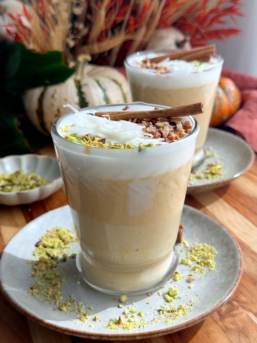Creamy pumpkin sahlab topped with coconut, chopped nuts, and cinnamon sticks.