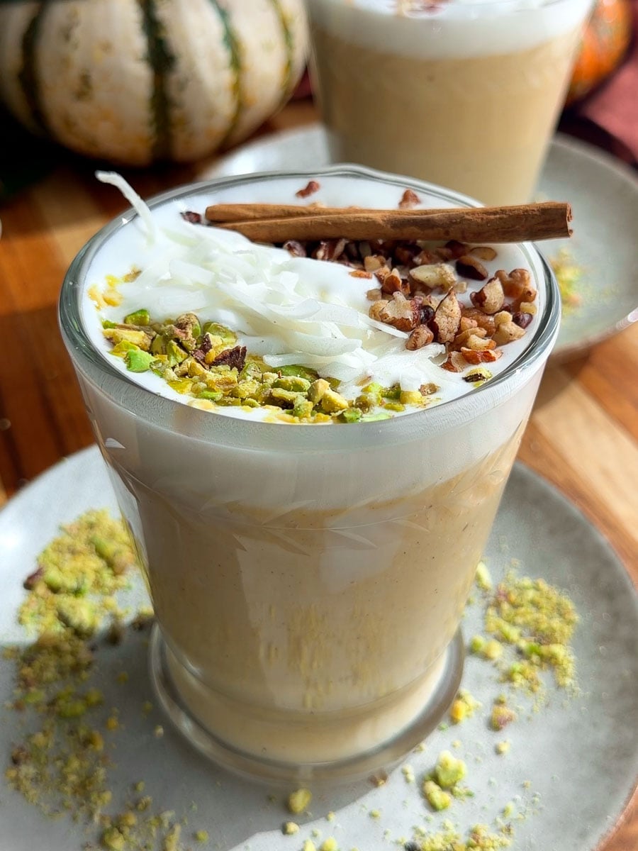 Creamy pumpkin sahlab topped with whipped cream, coconut, chopped nuts, and a cinnamon stick.