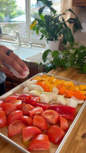 Seasoned chopped tomatoes, bell peppers, onions, and pumpkin on a baking sheet.